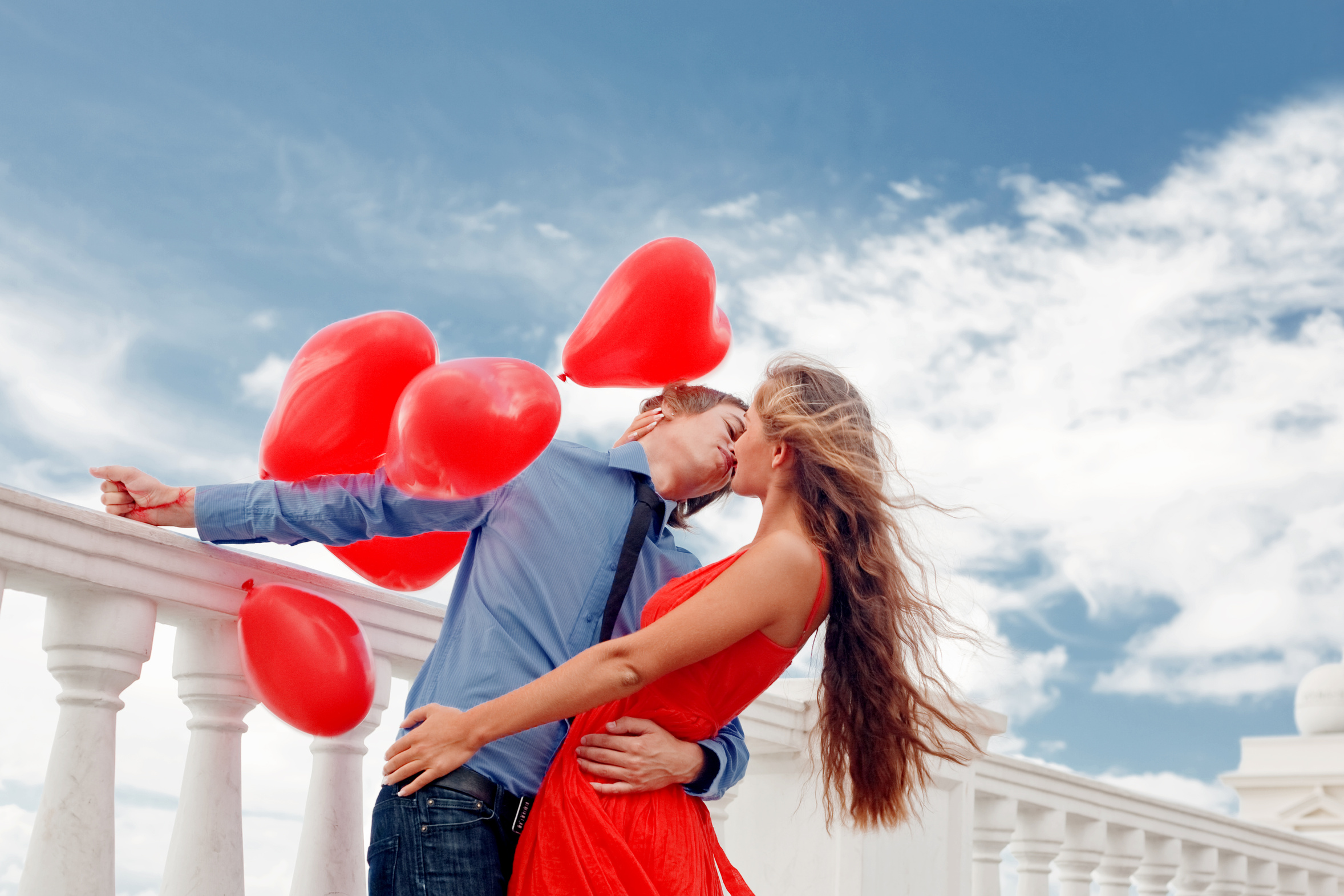 Teenage couple embracing over sky and holding bunch of baloons-hearts